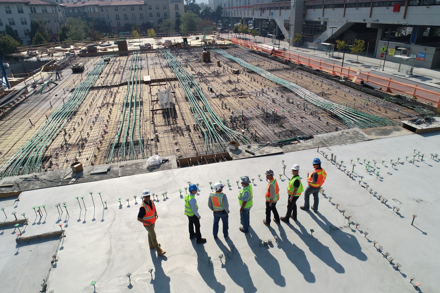 Group of construction workers standing on the rooftop of a building, overlooking the construction site below during daytime.